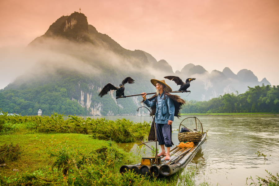 Pescador de cormoran sobre una lancha en el rio Yulong en Yanshuo, China